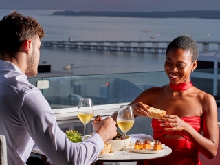 A Man And Woman Eating At A Table With A View Of The Ocean