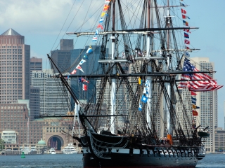 A Large Sailboat In A Harbor With USS Constitution In The Background