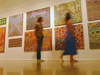 A Couple Of People Walking In A Room With Art On The Wall