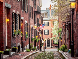 A Brick Street With Brick Buildings And A Flag On The Side With Beacon Hill In The Background