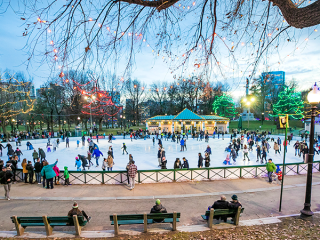 A Group Of People Walking Around A Park With Trees And Lights